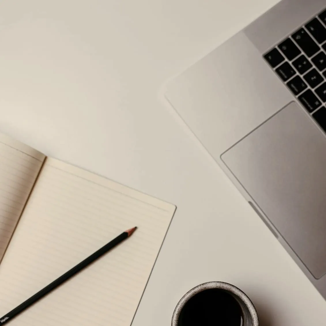 Ordinateur portable, carnet ouvert et crayon posés sur un bureau clair