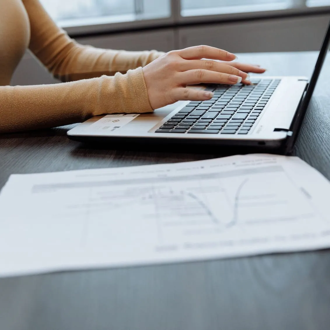 Une main sur le clavier d’un ordinateur portable, à côté d’un document imprimé